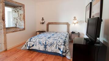 A bedroom with a wooden floor, a bed with a patterned bedspread, a television, and a stone wall.