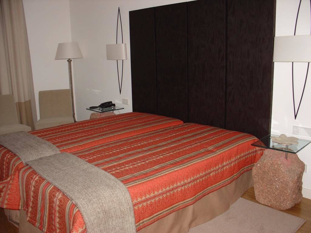 A bedroom with a large bed, a bedside table with a lamp, and a dark headboard.
