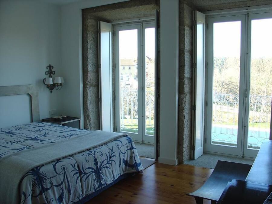 Un dormitorio con cama, mesita de noche, escritorio y un amplio ventanal con vistas al exterior.