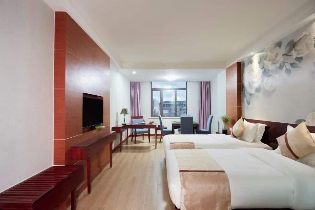 Ein Hotelzimmer mit Fernseher, zwei Betten, einem Schreibtisch und einem Stuhl.