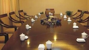 Un salón de conferencias con una mesa larga, sillas y un centro de mesa floral.