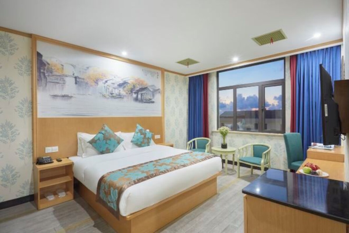 A hotel room with a large bed, a desk, a chair, a small table, and a window with curtains.