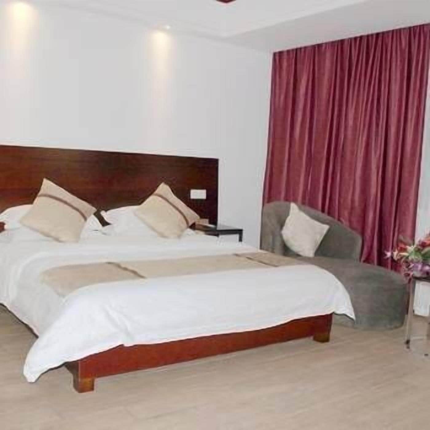 A hotel room with a double bed, a nightstand, a chair, and a large window with red curtains.