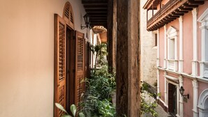 A narrow alleyway with wooden doors and balconies, surrounded by lush greenery. - Casa del Arzobispado Hotel (Cartagena)