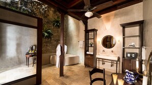 A bathroom with a stone wall, a bathtub, a vanity with a mirror, and a ceiling fan. - Casa del Arzobispado Hotel (Cartagena)