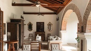 A spacious living area with a high ceiling, exposed wooden beams, and a fireplace. There are several seating areas with upholstered chairs and a sofa. - Casa del Arzobispado Hotel (Cartagena)