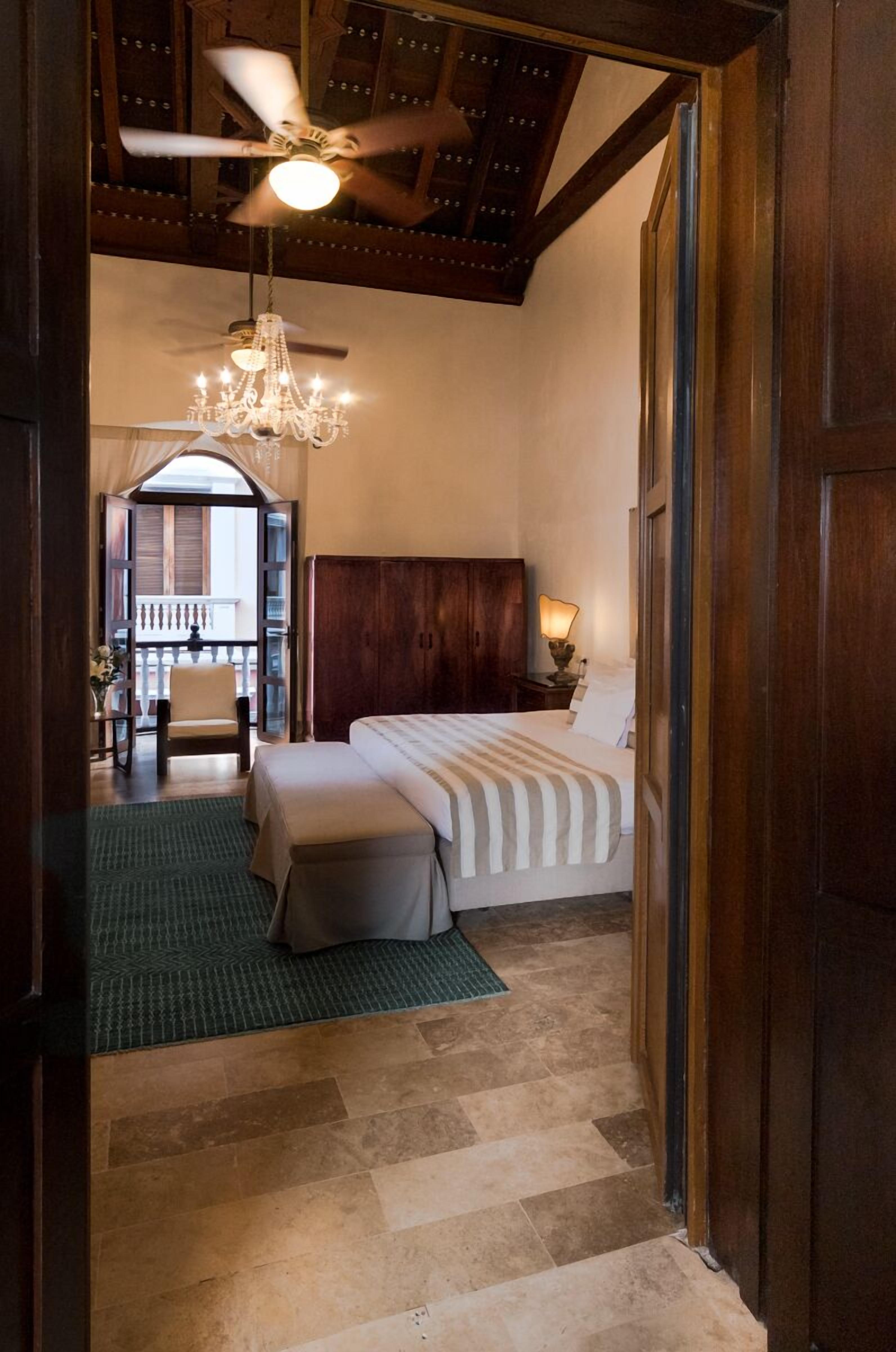 Une chambre avec un grand lit, un lustre, un ventilateur de plafond et une vue sur un balcon.