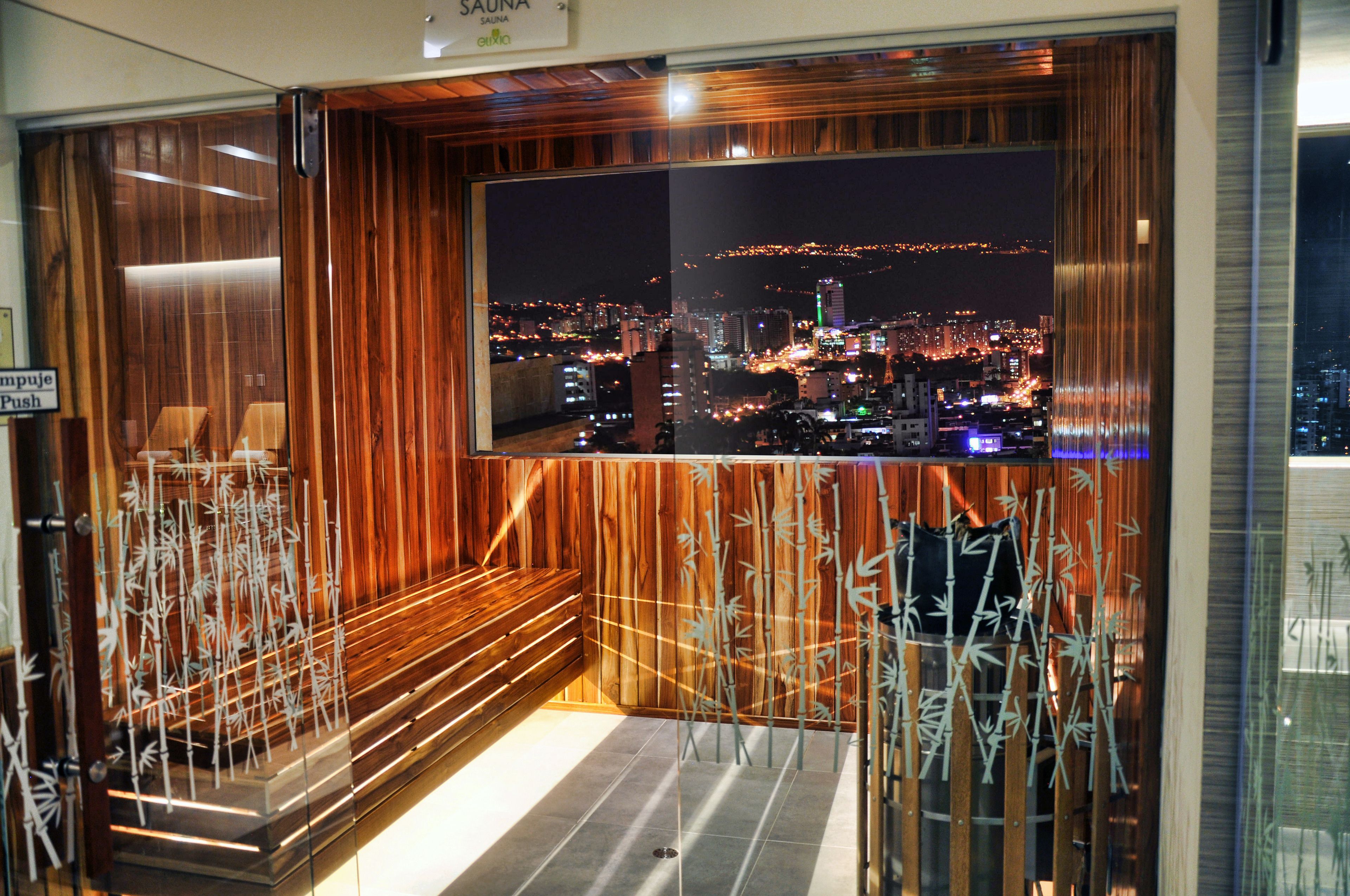 A room with a large window overlooking a cityscape at night, wooden paneling, and a bench.