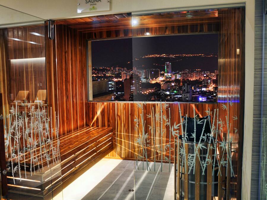 A room with a large window overlooking a cityscape at night, wooden paneling, and a bench.