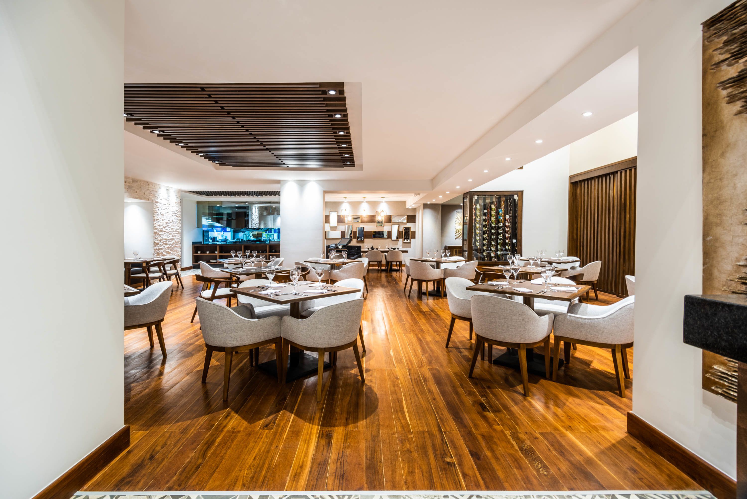 A spacious restaurant with wooden flooring, multiple dining tables, and chairs.