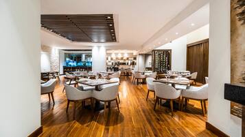 A spacious restaurant with wooden flooring, multiple dining tables, and chairs.
