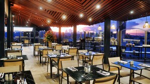 A restaurant with tables and chairs, a wooden ceiling, and a view of the cityscape at sunset. - Hotel Dann Carlton Bucaramanga (Bucaramanga)
