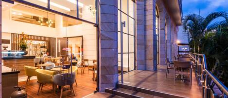 A modern hotel lobby with a spacious seating area, a staircase leading to an upper level, and a view of the outdoors.