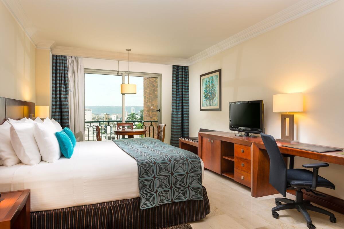 Ein Hotelzimmer mit Bett, Schreibtisch, Fernseher und Balkon.
