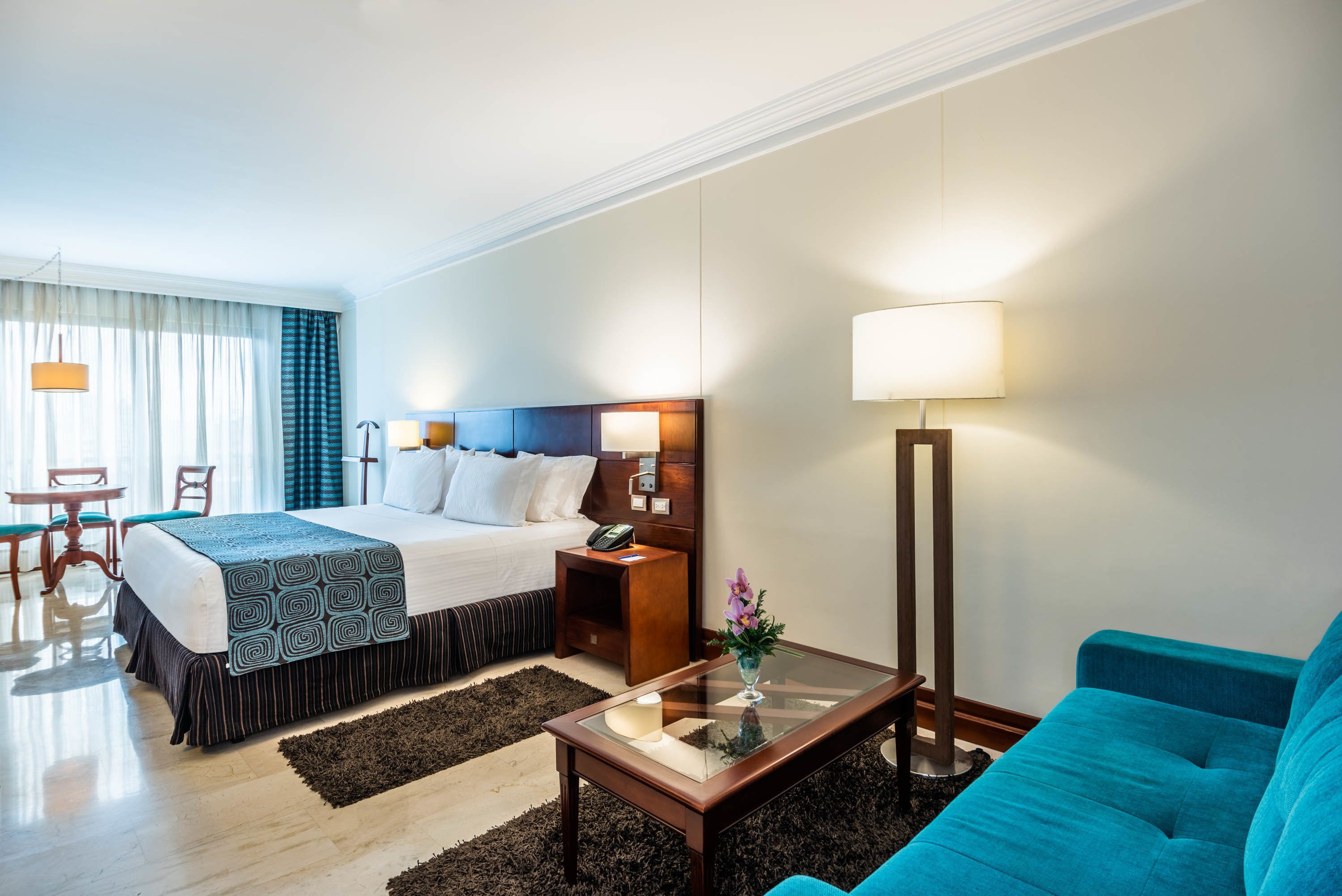 Una habitación de hotel con cama, mesita de noche, lámpara y un sofá azul.