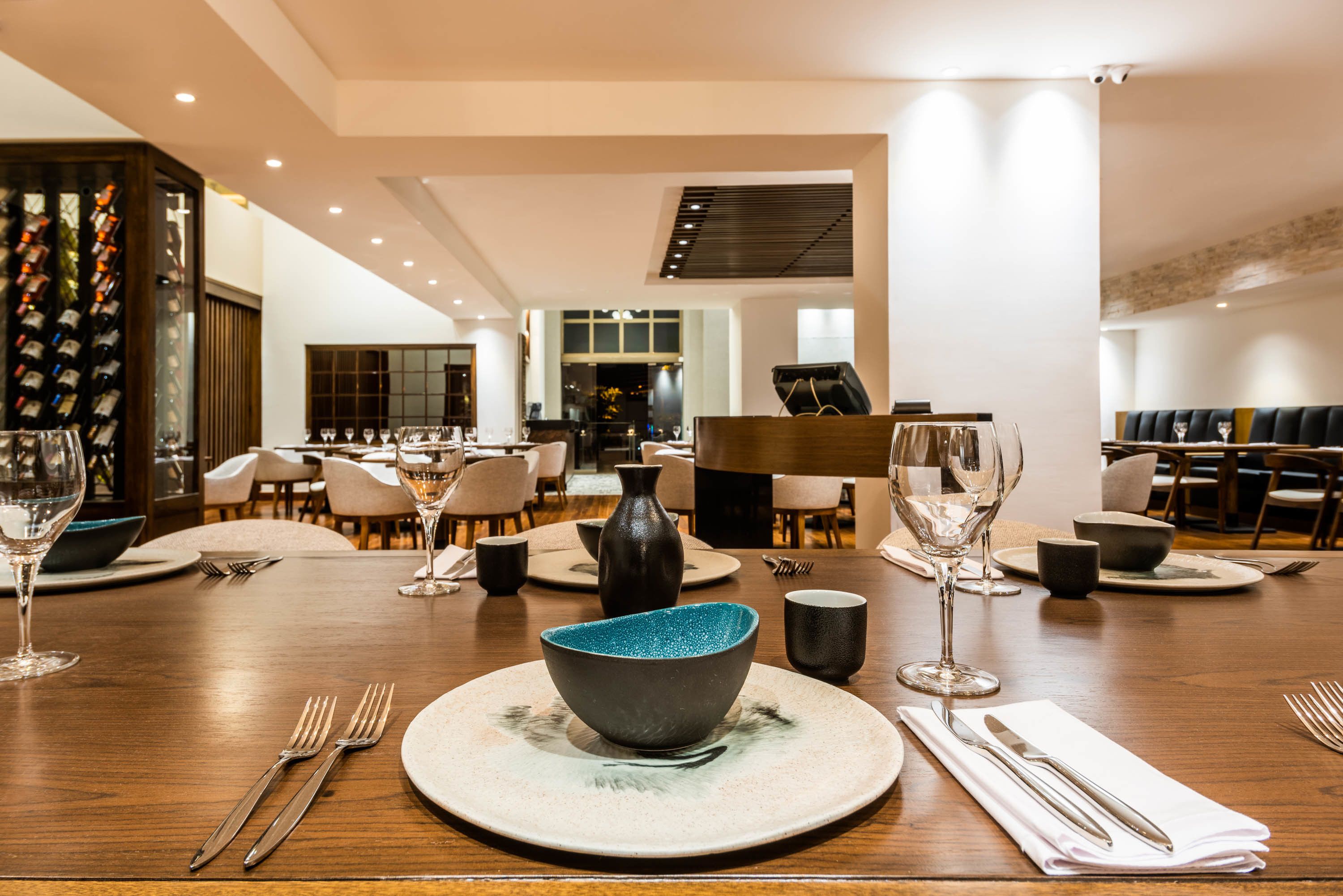 Un comedor con mesas dispuestas para una comida, incluyendo platos, tazones, cubiertos y vasos.