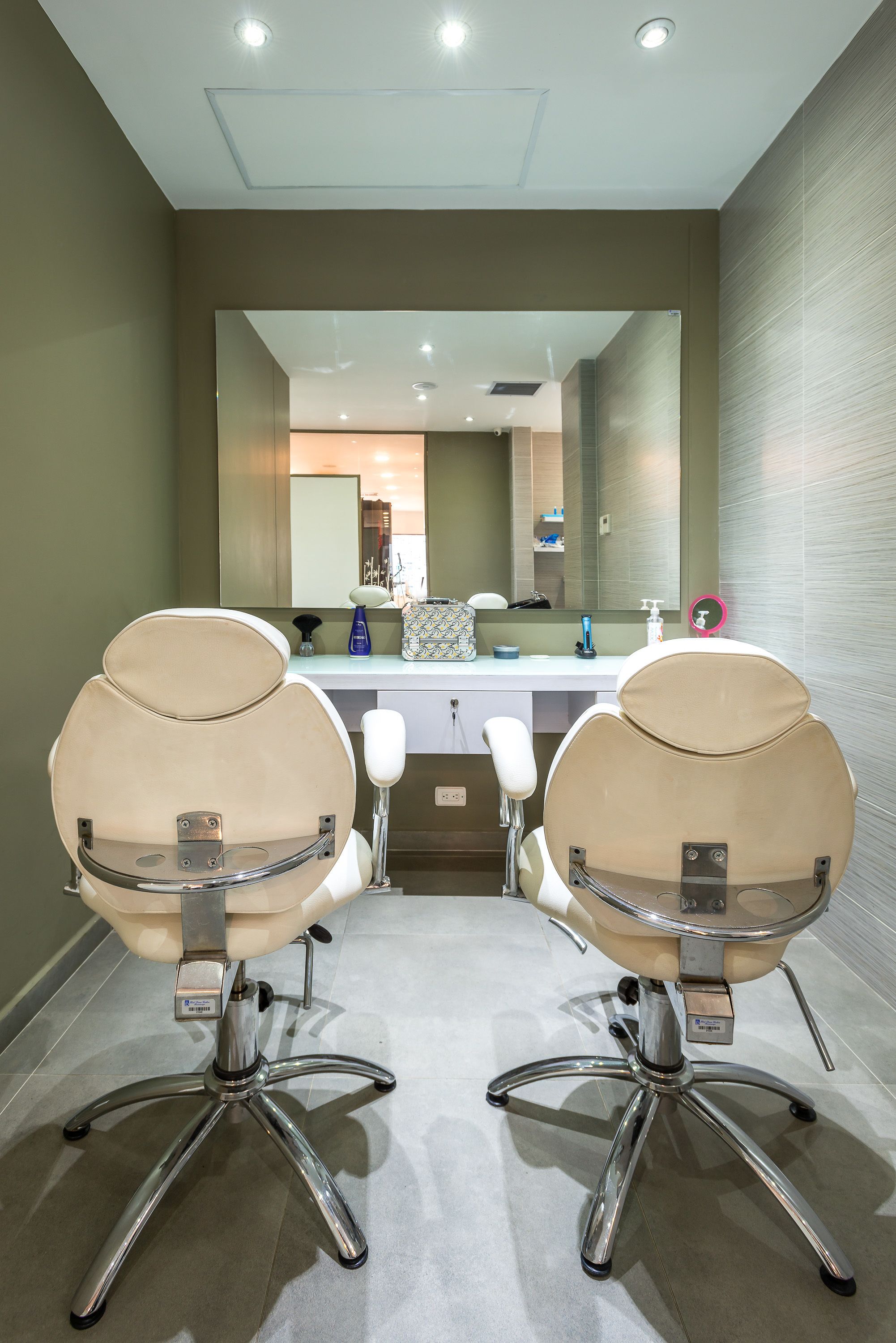 A modern bathroom with two beige chairs, a large mirror, and a white countertop with toiletries.