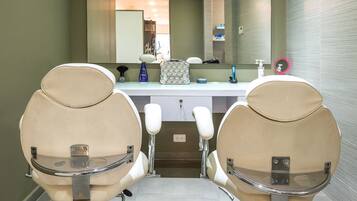 Un baño moderno con dos sillas color beige, un espejo grande y una encimera blanca con artículos de aseo.