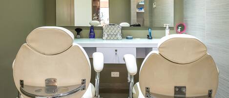 A modern bathroom with two beige chairs, a large mirror, and a white countertop with toiletries.