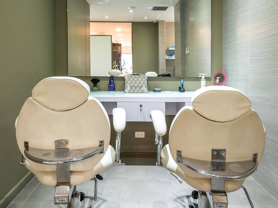 Un baño moderno con dos sillas color beige, un espejo grande y una encimera blanca con artículos de aseo.