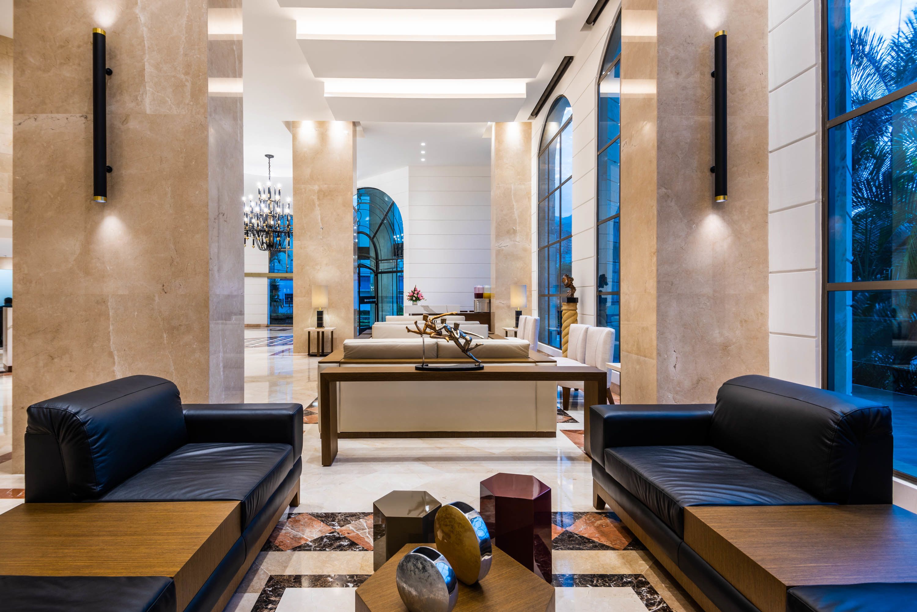 A modern lobby with a central seating area, large windows, and a chandelier.