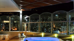 A rooftop terrace with a hot tub, wooden flooring, and a city view at night. - Hotel Dann Carlton Bucaramanga (Bucaramanga)