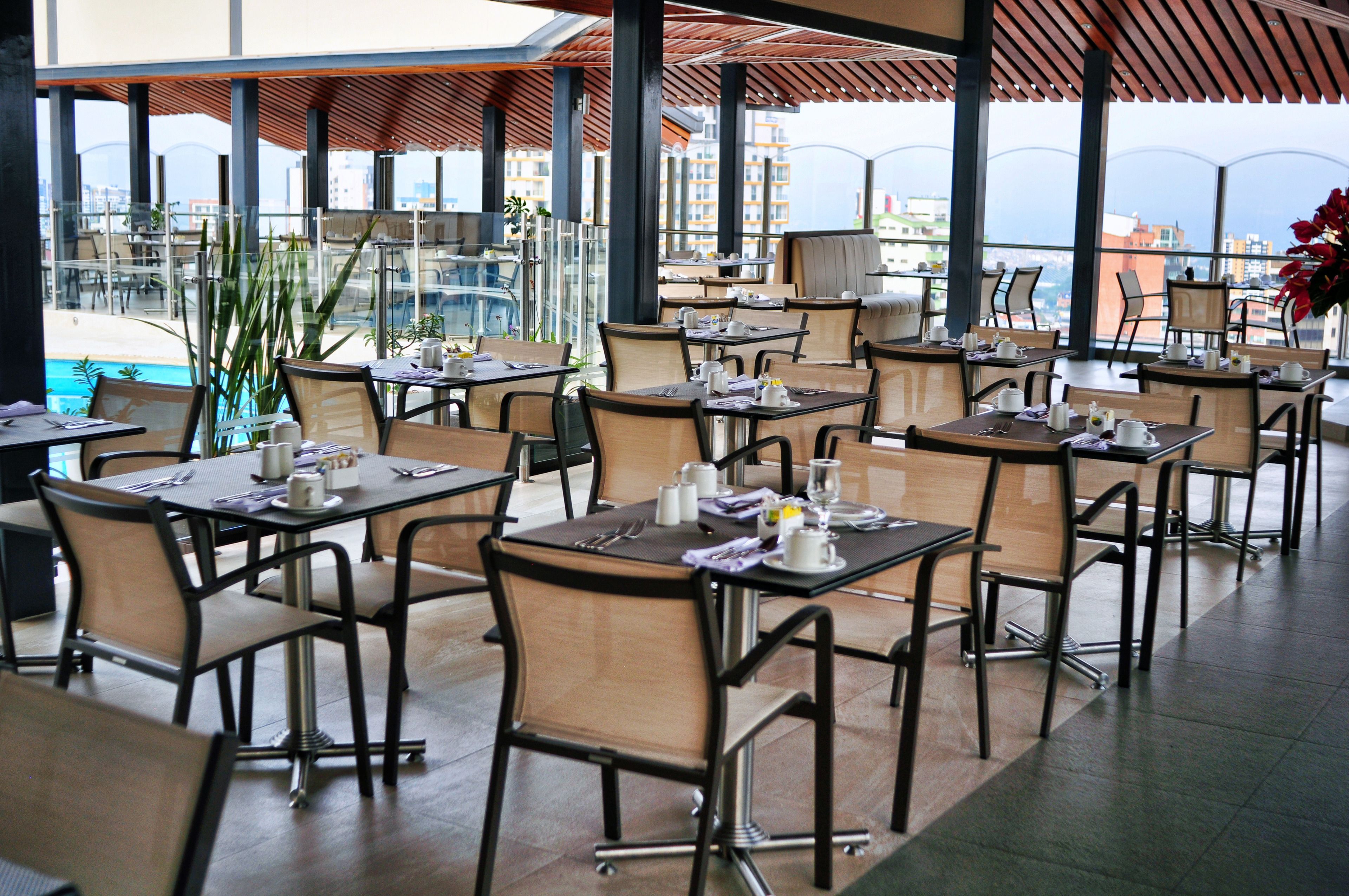 A restaurant with multiple tables and chairs, large windows, and a view of the cityscape.