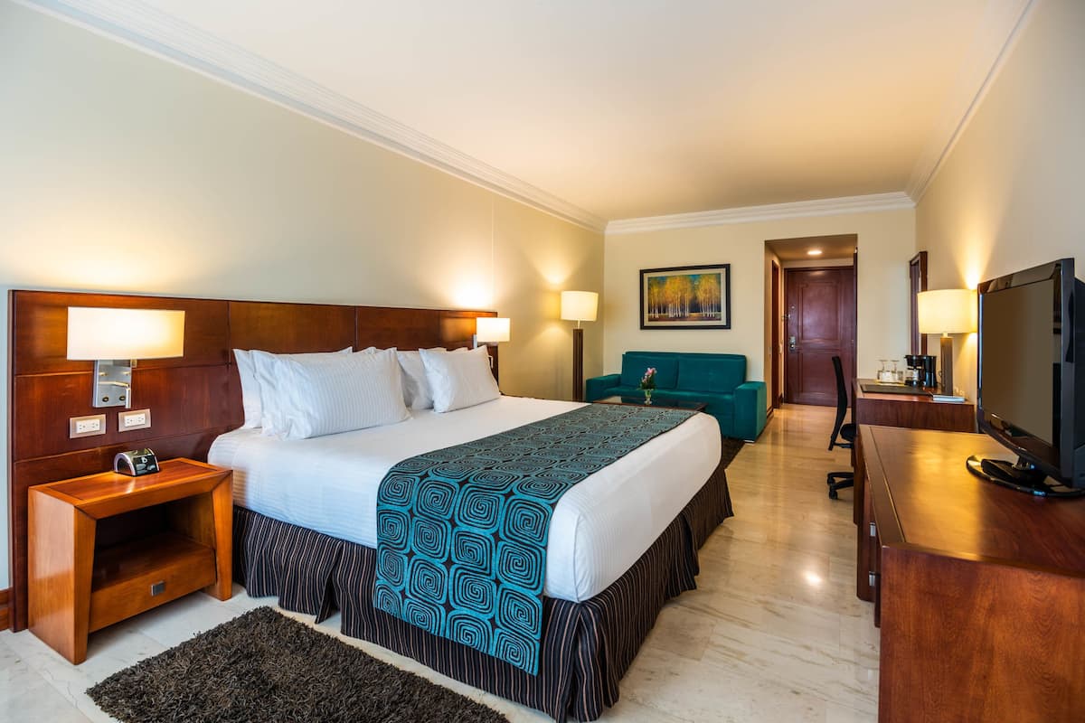 Ein Hotelzimmer mit einem großen Bett, Nachttischen, einem Schreibtisch, einem Fernseher und einem Bild an der Wand.