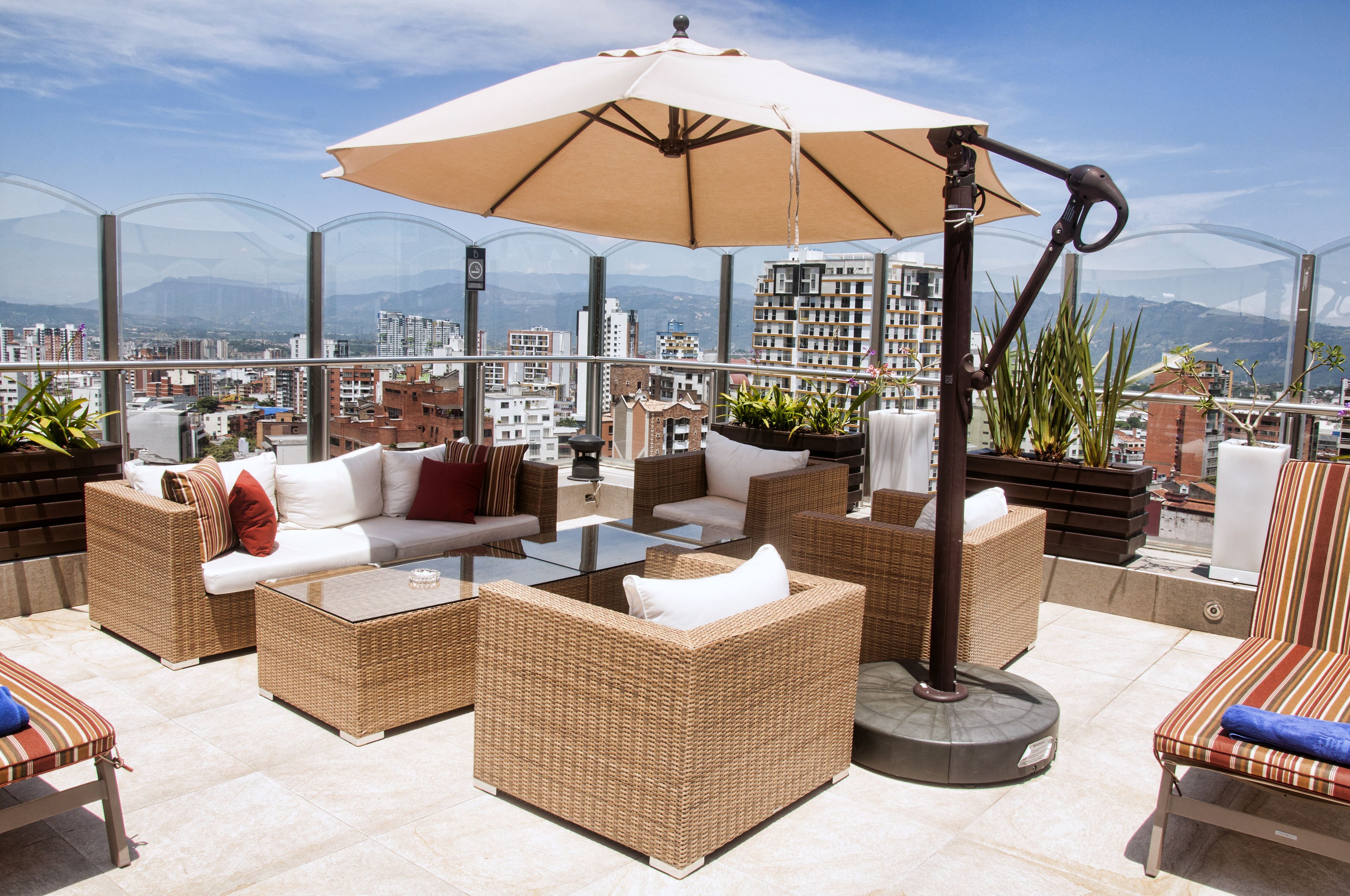 Una terraza en la azotea con mobiliario de mimbre, una mesa de vidrio y un paraguas grande.