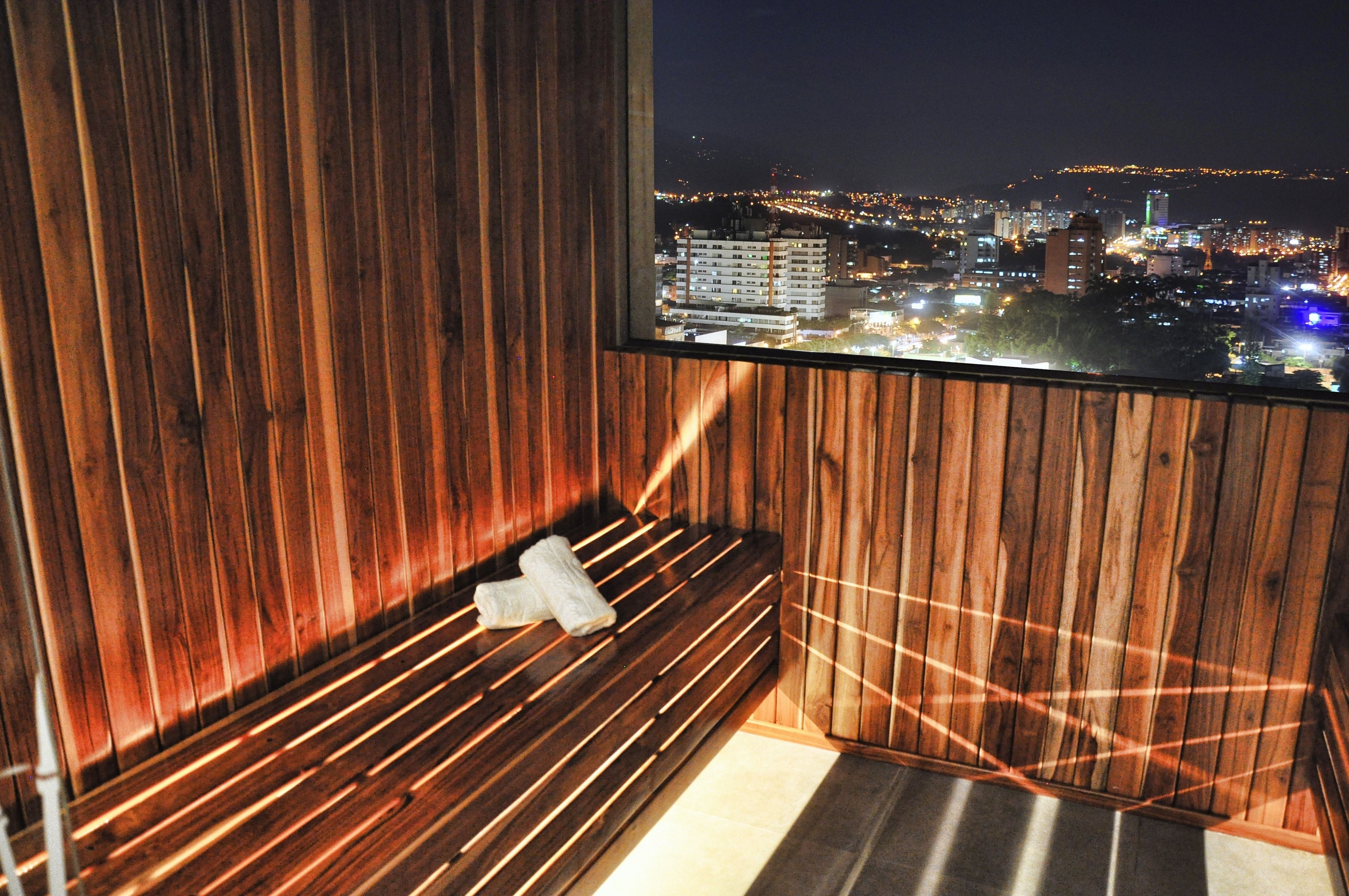 A wooden sauna with a bench and a towel, a window with a cityscape view at night.