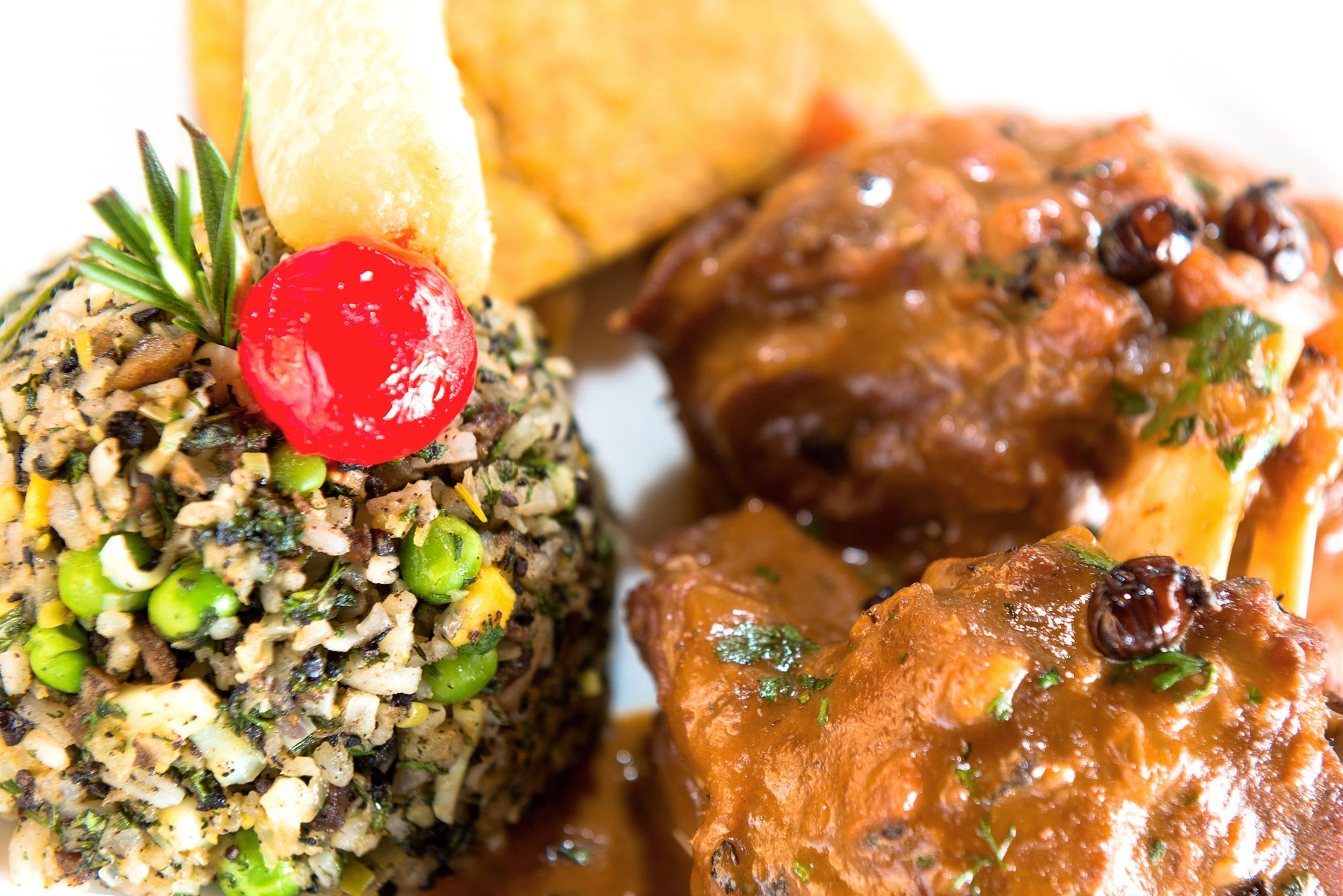 A plate with a mound of rice mixed with green peas and herbs, a piece of meat with sauce, and a cherry on top.