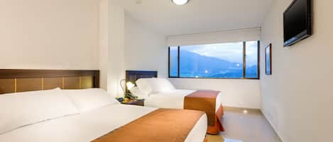 Habitación de hotel con dos camas, un televisor, una ventana con vista a las montañas y una mesita de noche con lámpara.