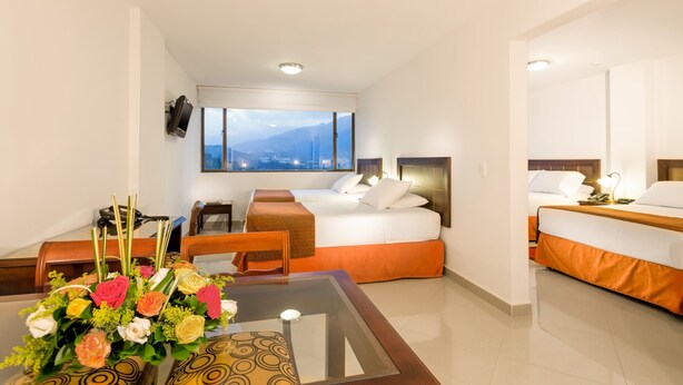 Una habitación de hotel con cama, escritorio, silla, mesa con un jarrón de flores y un gran ventanal con vistas a la montaña.