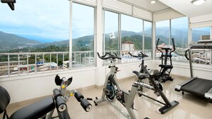 Un gimnasio con equipo de ejercicio, ventanas amplias y vistas a montañas.