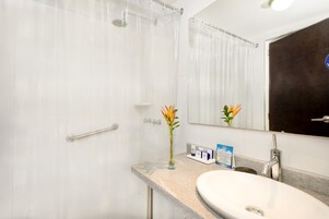 Un baño con ducha, lavamanos, espejo y un florero con flores.