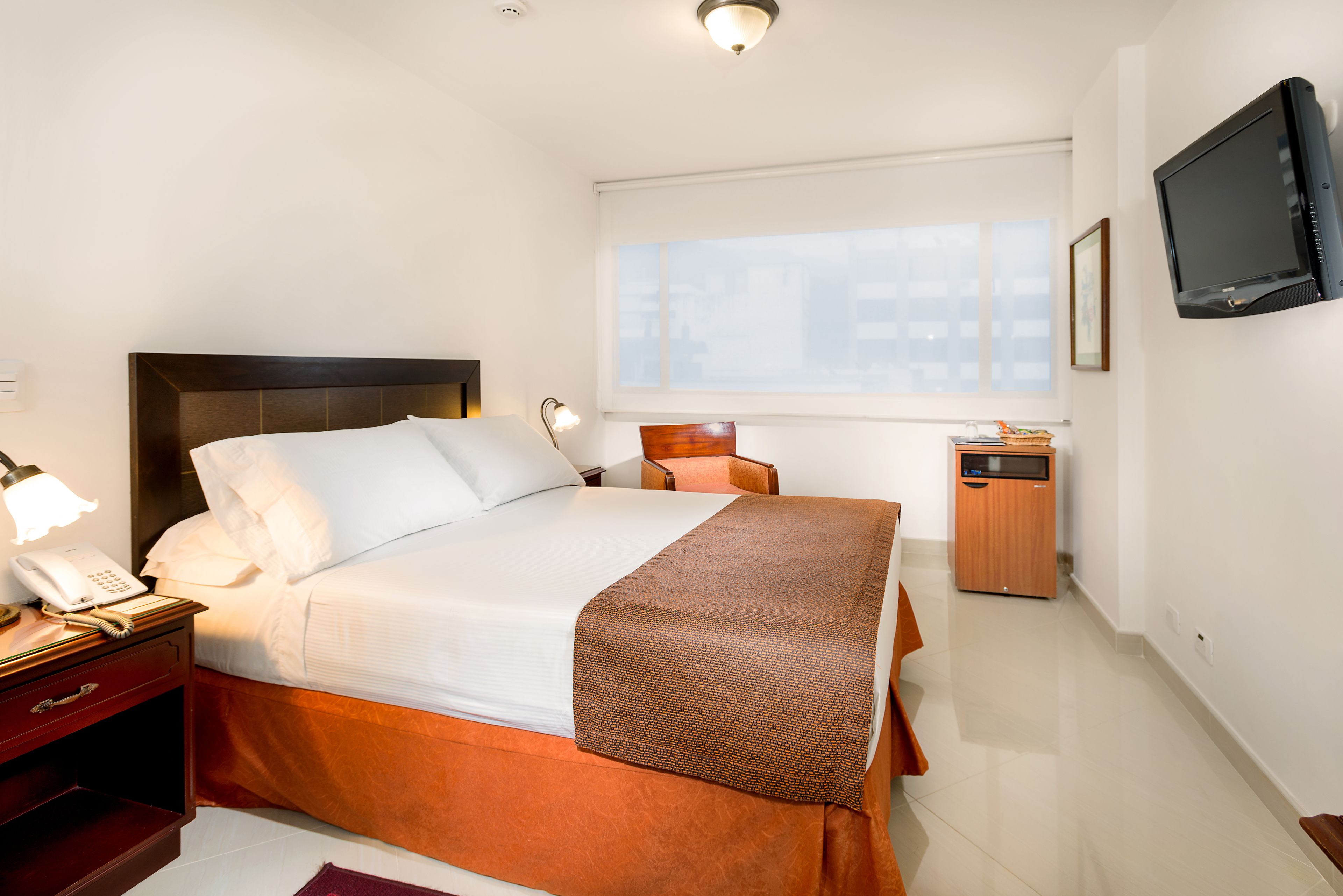 Habitación de hotel con cama, lámpara de noche, teléfono y televisión en la pared.