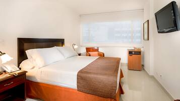 Habitación de hotel con cama, lámpara de noche, teléfono y televisión en la pared.