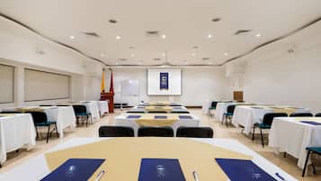 A conference room with tables set up for a meeting, a projector screen, and a presentation screen in the background.