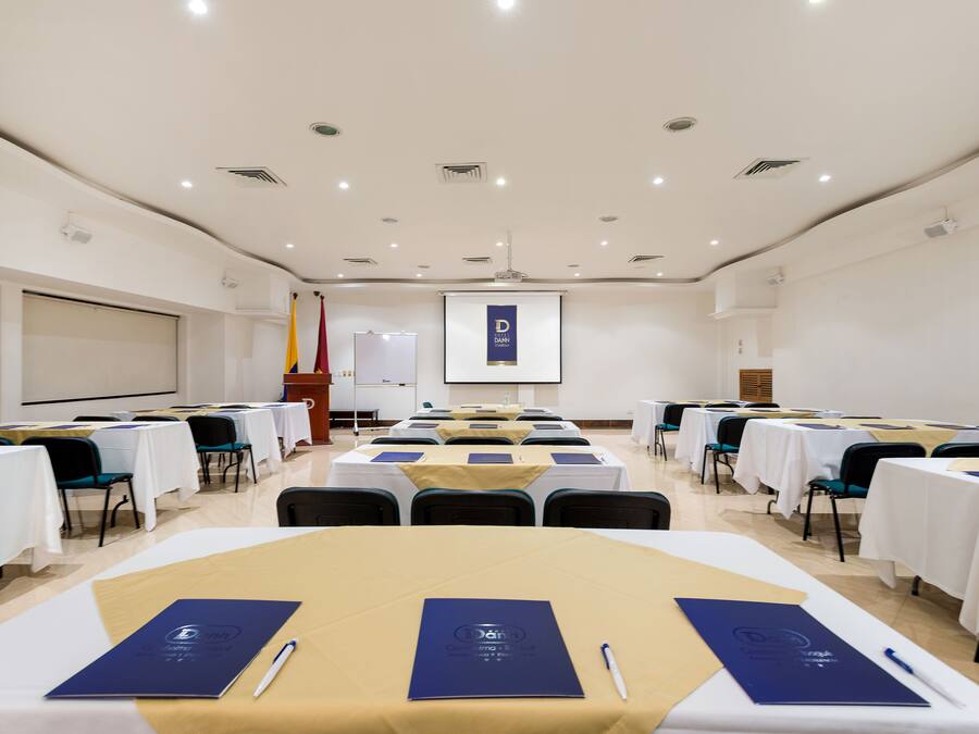 A conference room with tables set up for a meeting, a projector screen, and a presentation screen in the background.