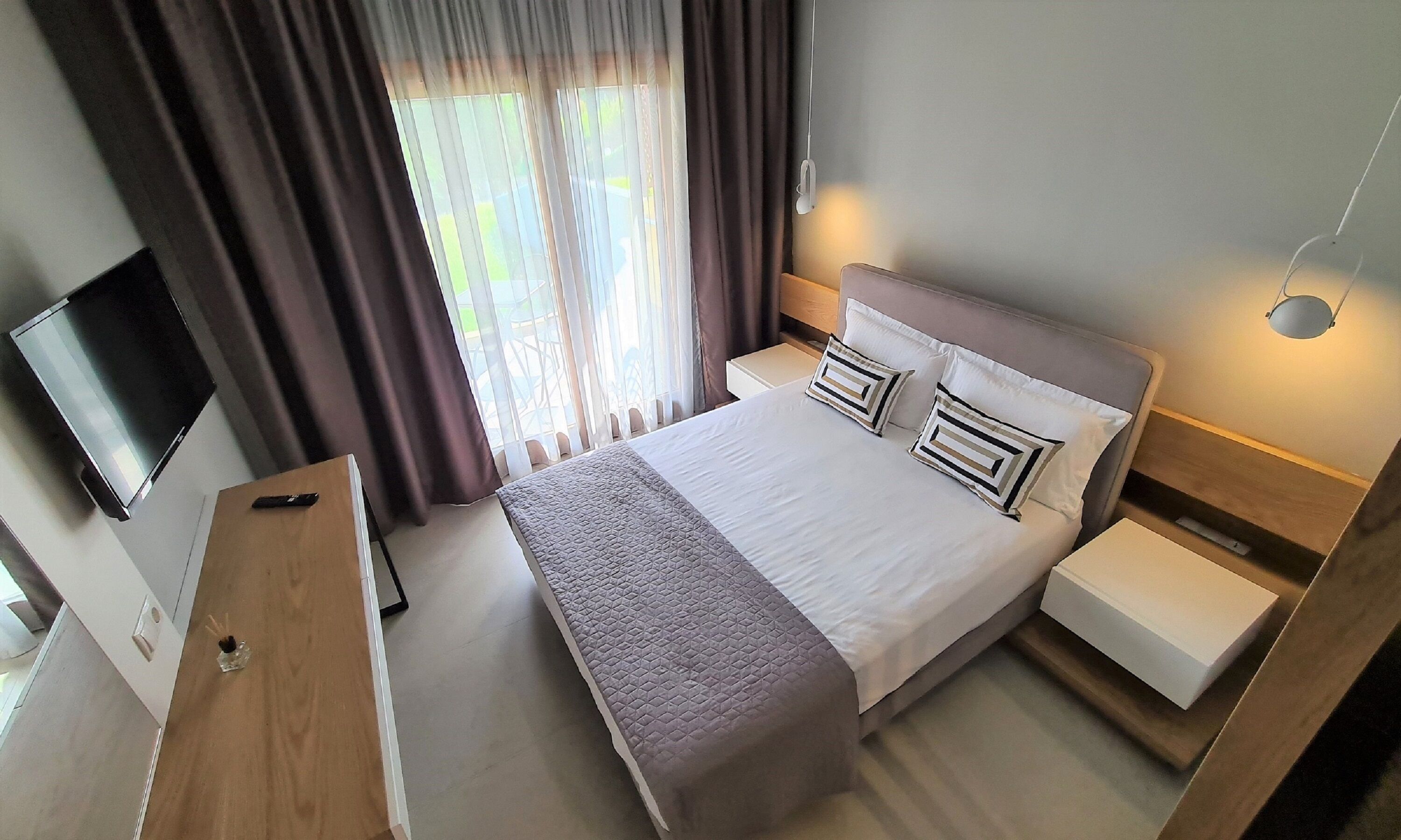 A hotel room with a bed, bedside tables, a TV, and a window with curtains.