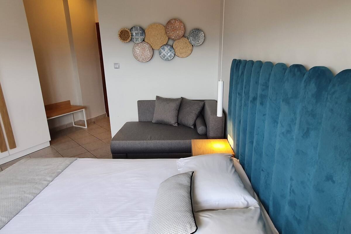 Ein Schlafzimmer mit Bett, Sofa, Wanddeko und einem blauen Vorhang.