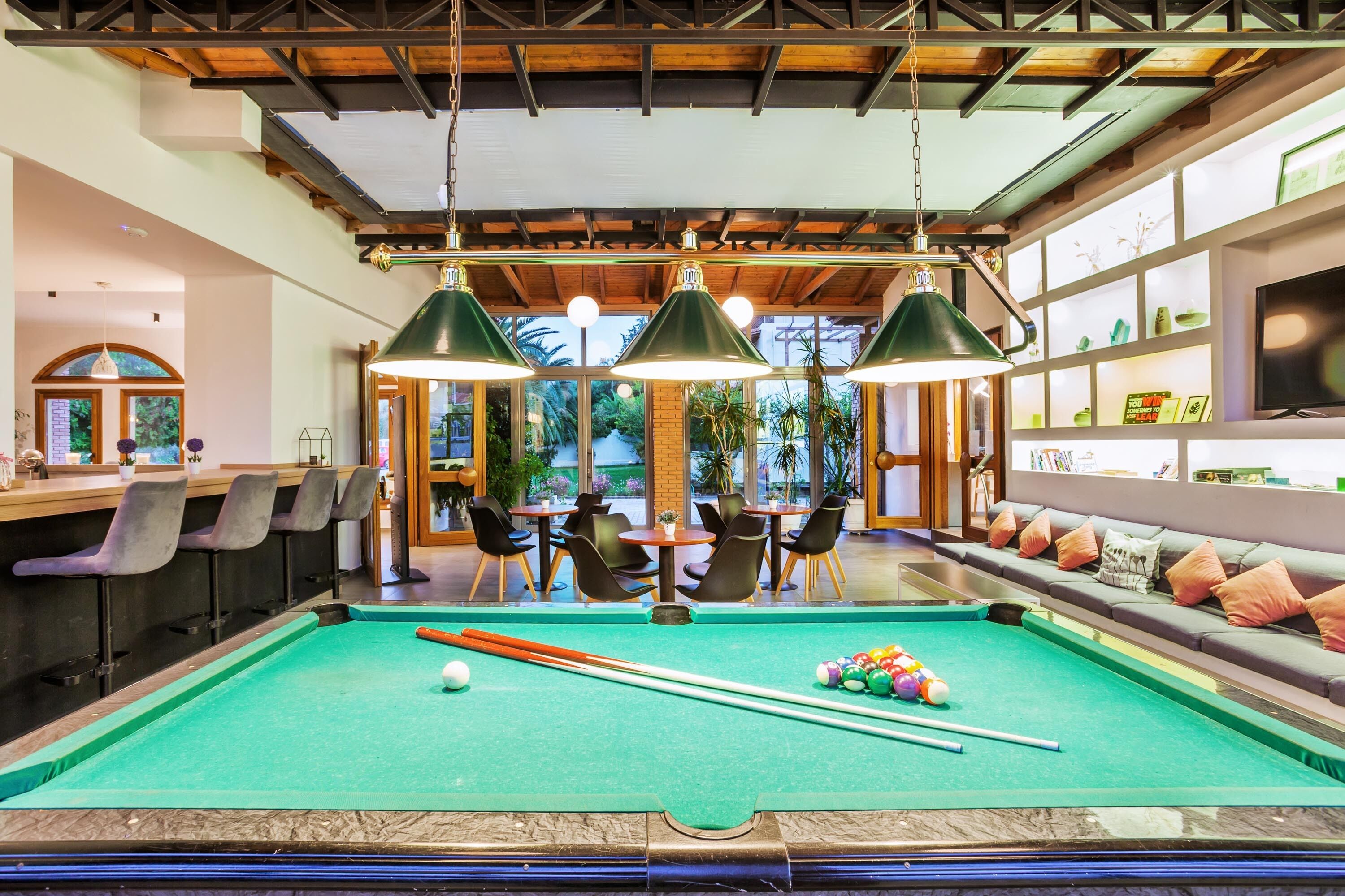 A pool table with green felt, surrounded by bar seating and a seating area with cushions.