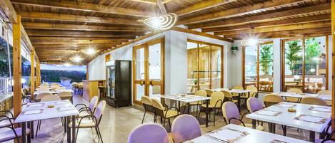 A restaurant with wooden beams and large windows, tables set with white tablecloths and chairs.