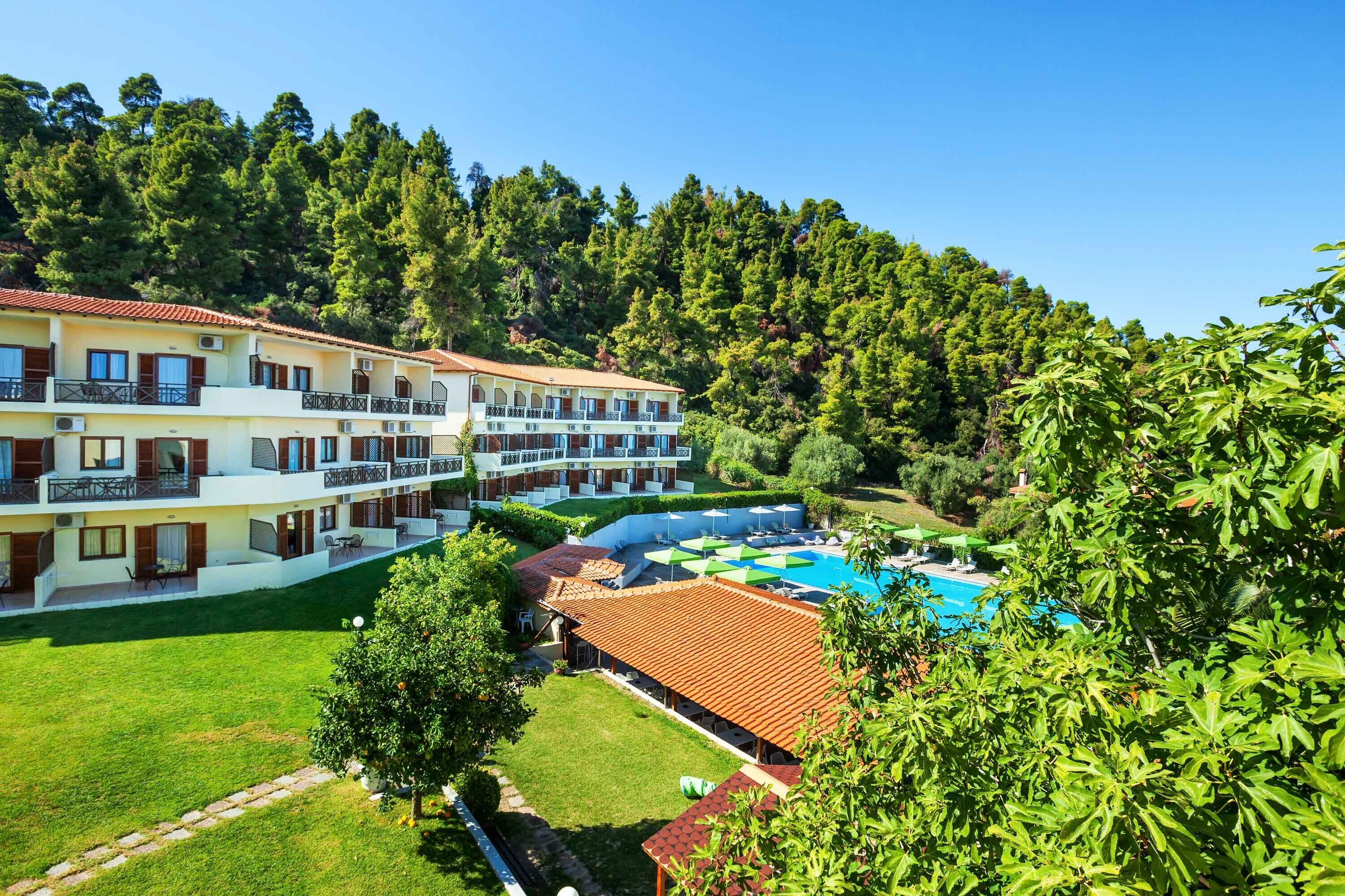 A hotel with multiple balconies, a swimming pool, and lush greenery.