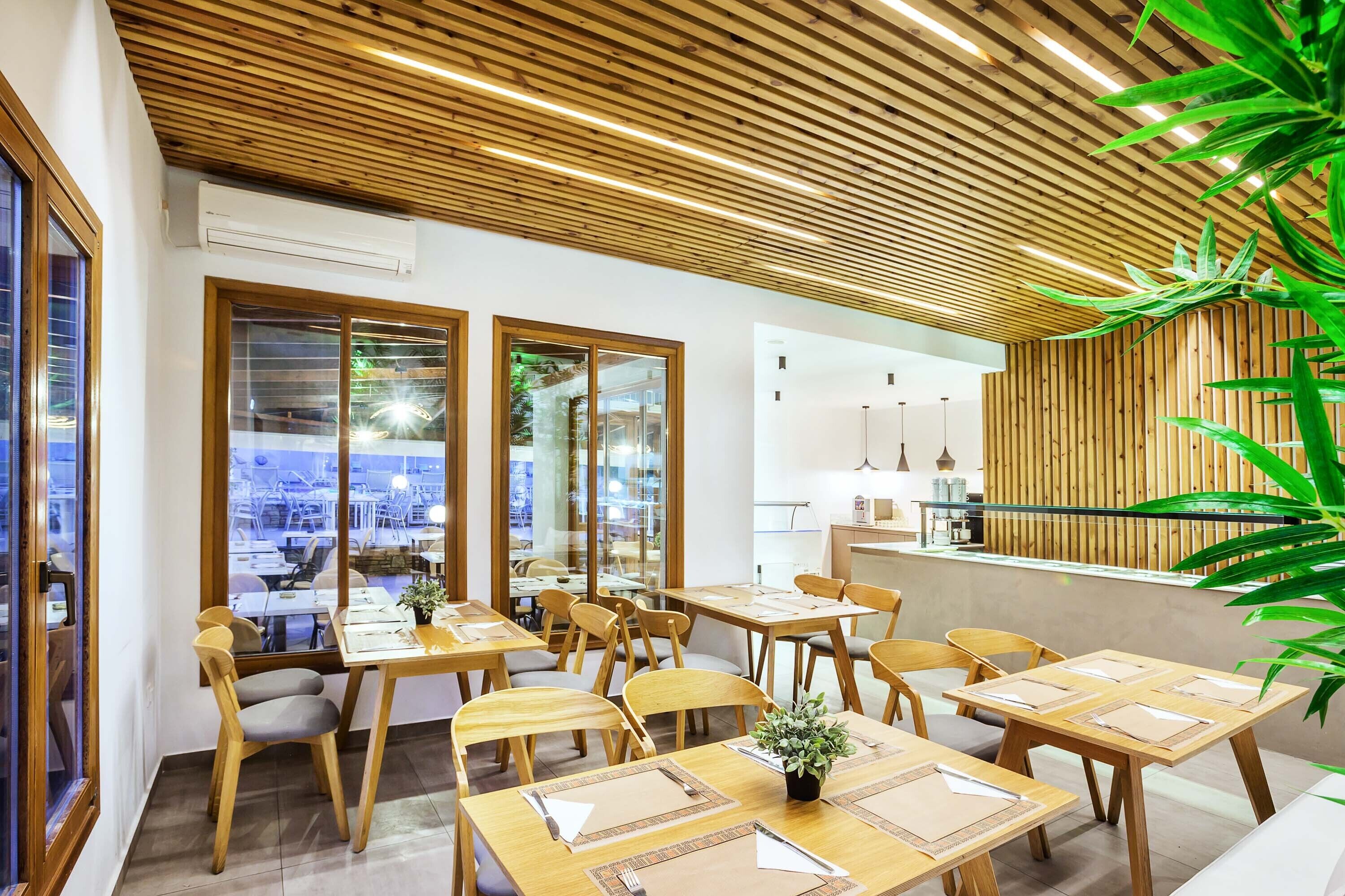 Un espace repas moderne avec des tables et des chaises en bois, de grandes fenêtres et un plafond en bois.
