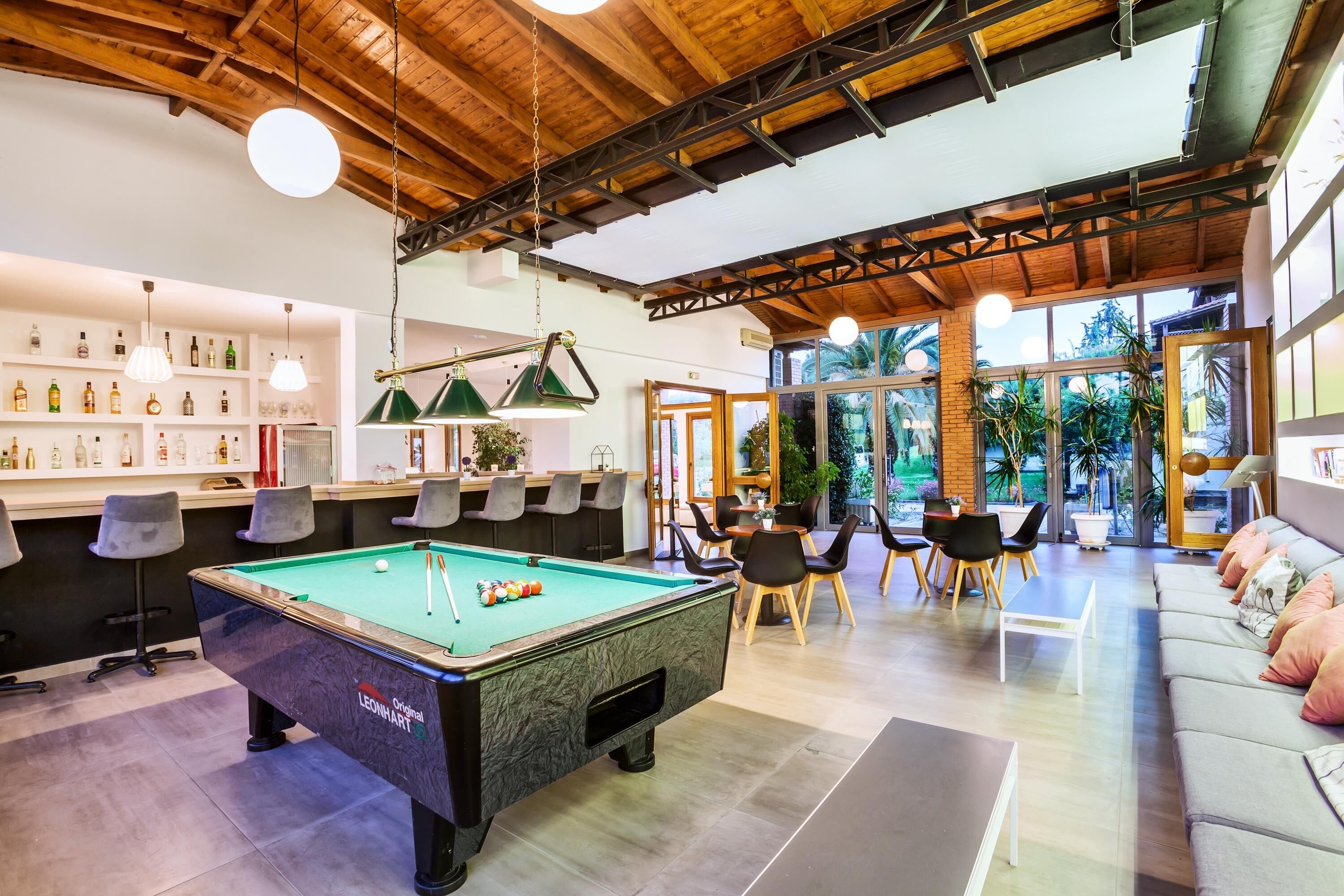 A pool table in a well-lit room with a bar area, seating, and large windows.