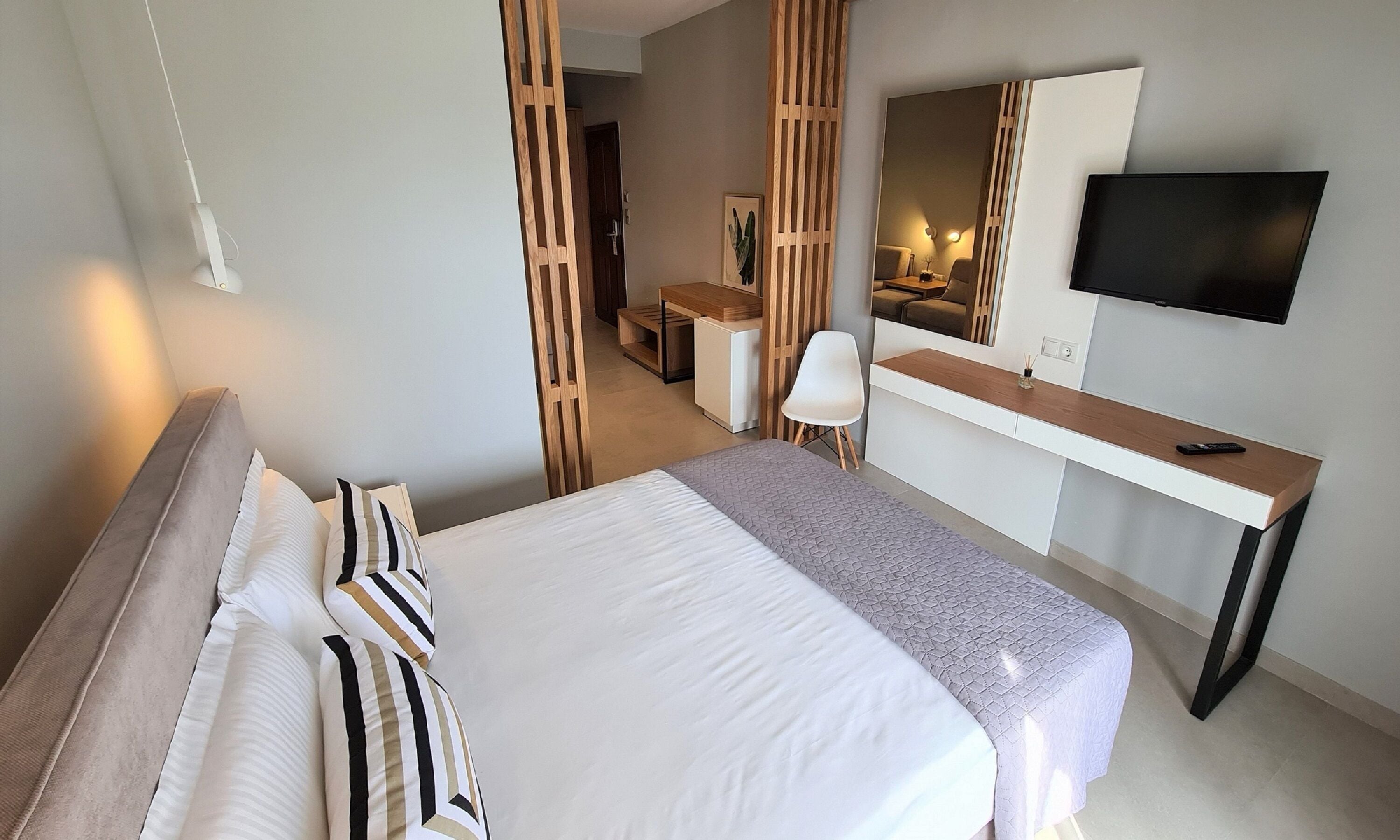 A hotel room with a bed, a desk, a chair, a TV, and a mirror.