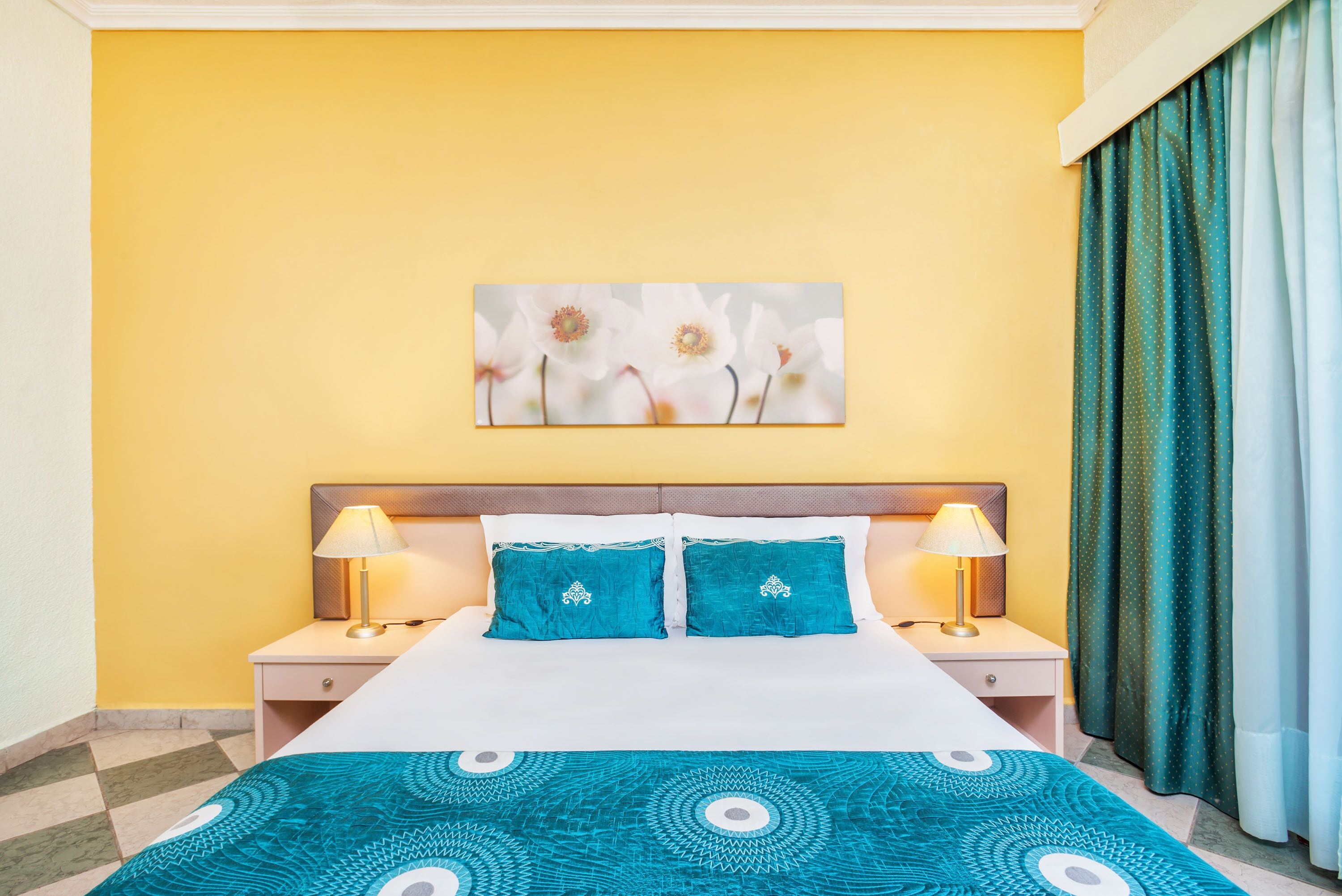 Een hotelkamer met een bed, twee nachtkastjes, een aan de muur hangend kunstwerk en een bedsprei met dessin.