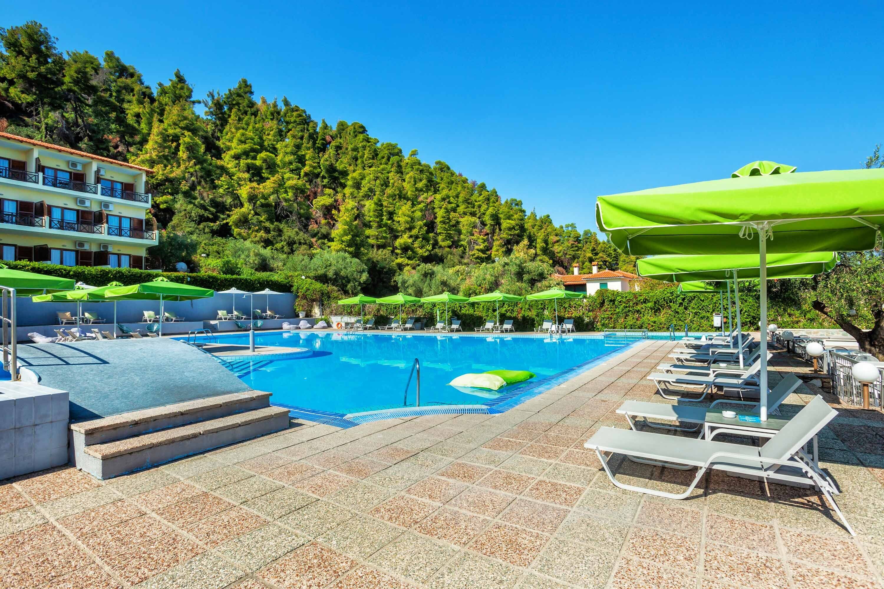 A swimming pool with lounge chairs and umbrellas, surrounded by a building and trees.