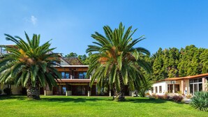 A two-story building with a balcony, surrounded by well-maintained grass and palm trees. - Palladium Hotel (Kassandra)